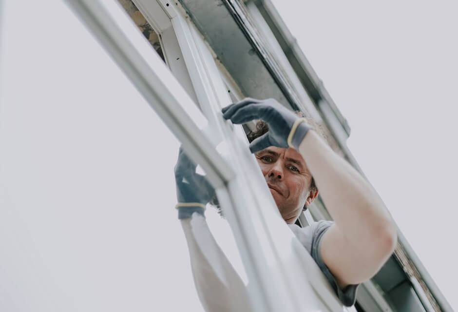 Worker inspecting a window frame from the outside, highlighting the issue of a leaking window and the need for proper sealing or repair.
